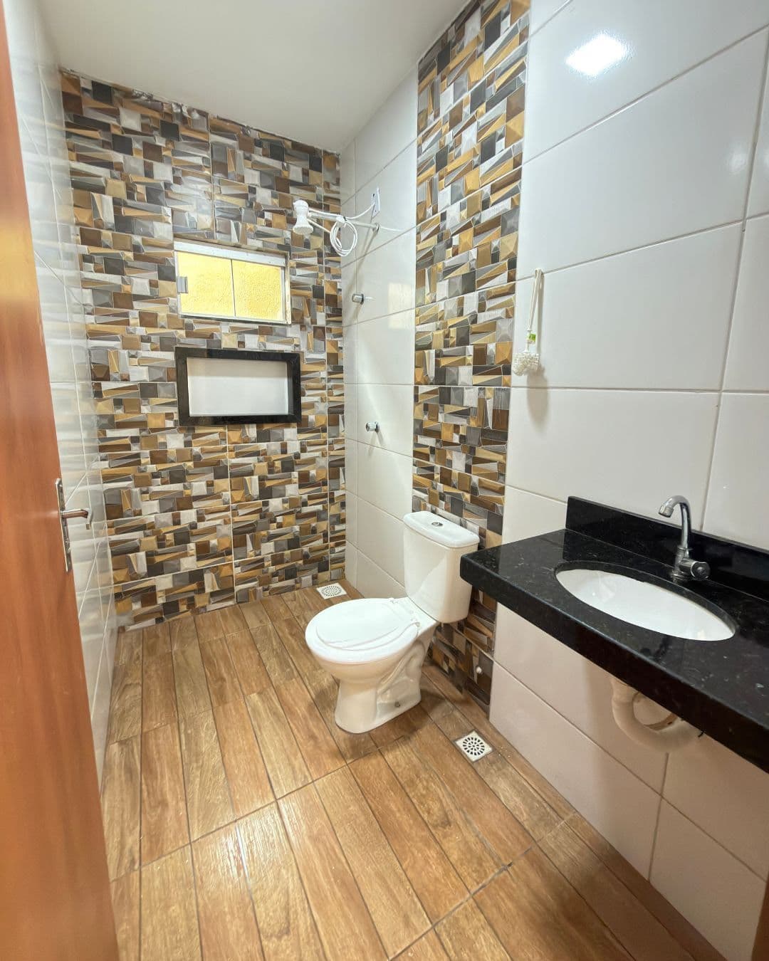 Banheiro social revestido do piso ao teto, bancada de granito preto com cuba embutida e piso amadeirado.