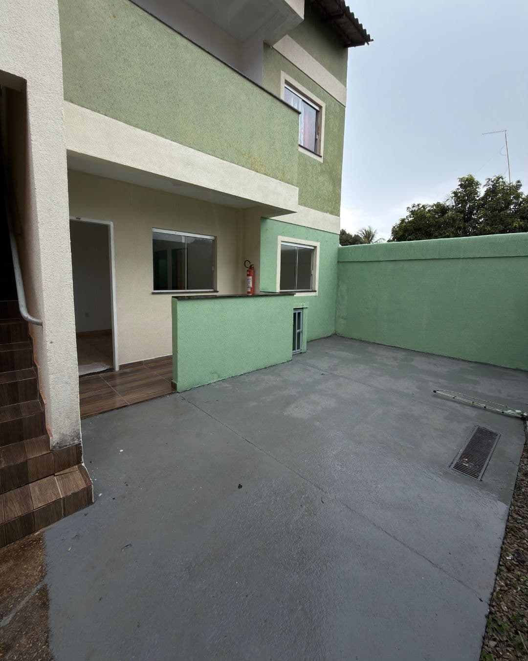 Quintal privativo do apartamento térreo, com piso cimentado, muro alto pintado de verde-sálvia e a fachada do sobrado ao fundo.